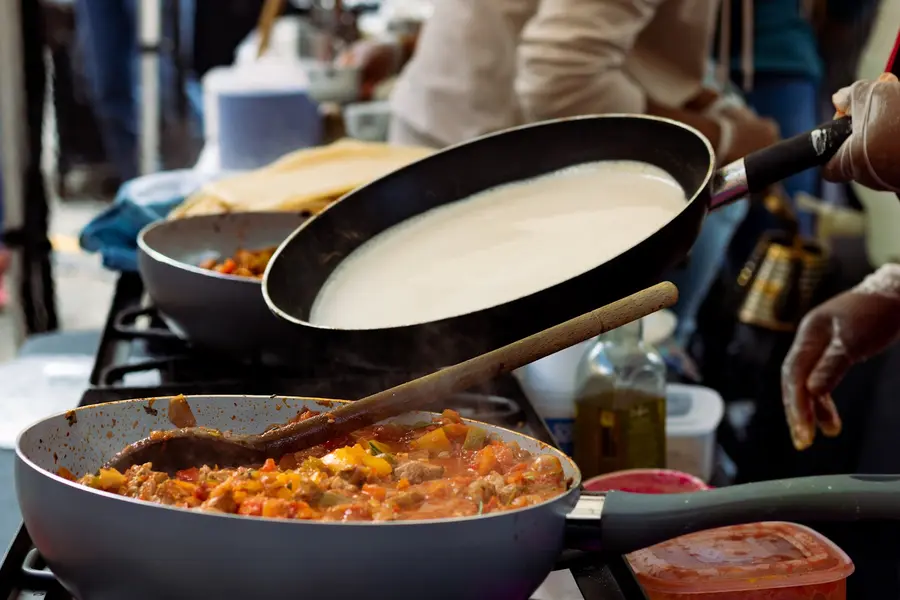 Injera cooking in a pan beside a stew at a street food market stall